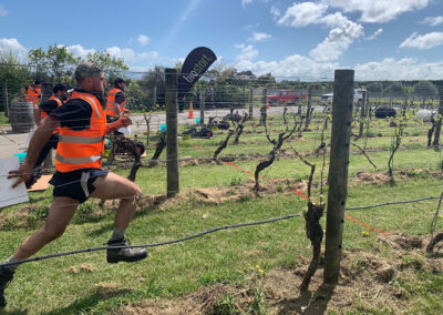 Four Hortisports competitors in hi-vis vests run between the vines in a vineyard as a part of a challenge.